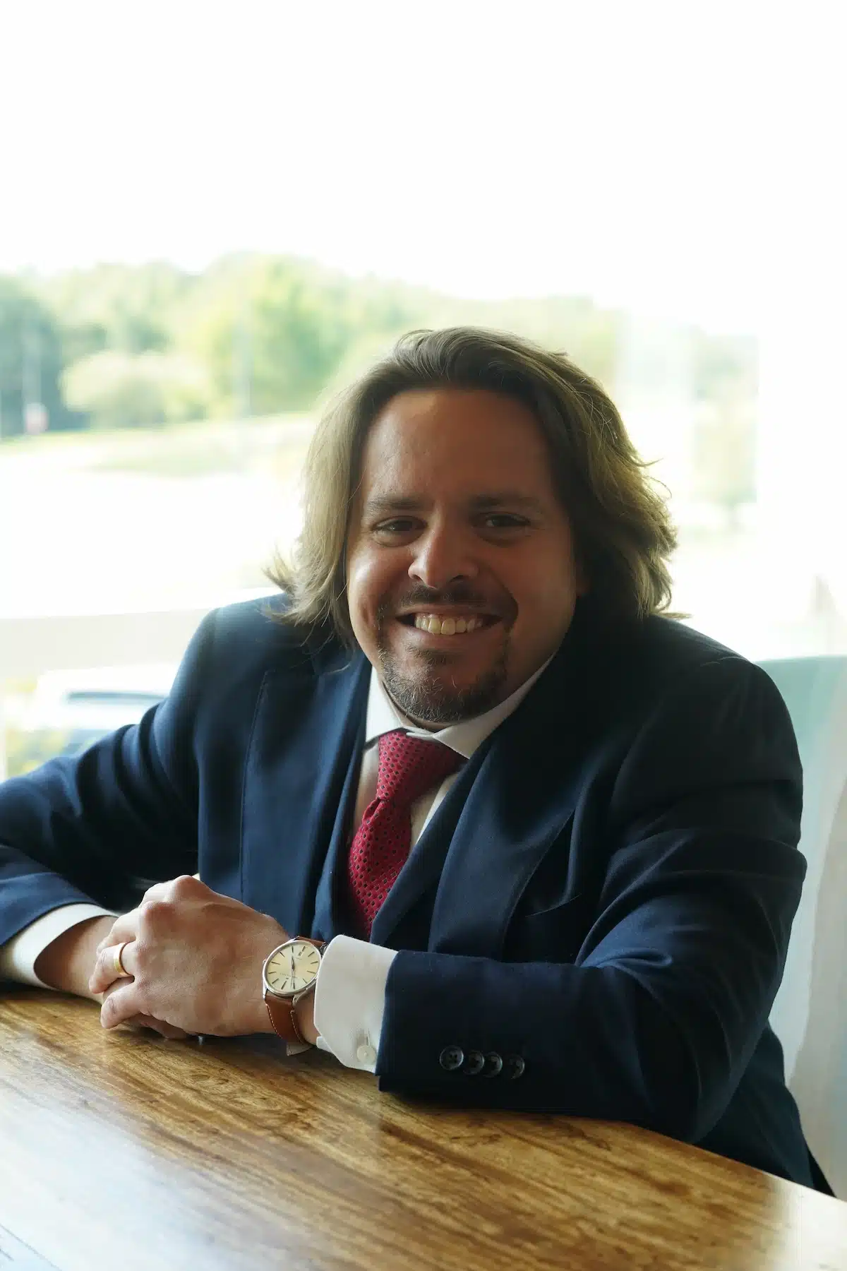 Vincent Massaro, personal injury attorney at Massaro Law, sitting at a wooden table with hands clasped, wearing a blue suit and red tie.